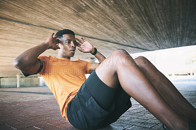 Buy stock photo Shot of a young man doing sit ups against an urban background