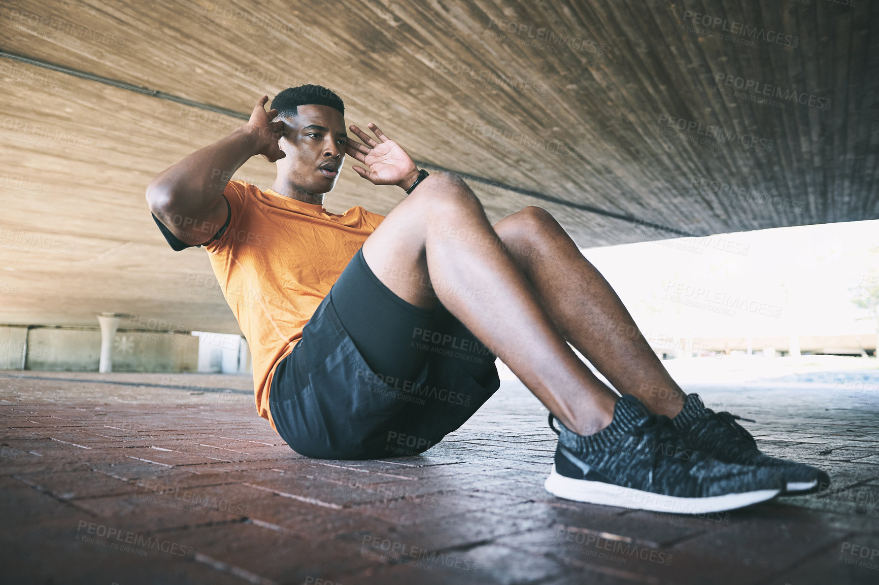 Buy stock photo Shot of a young man doing sit ups against an urban background