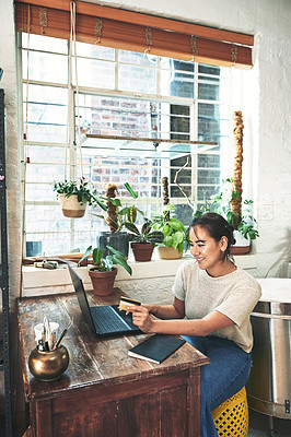 Buy stock photo Cropped shot of an attractive young business owner sitting alone in her studio and using her laptop for online shopping