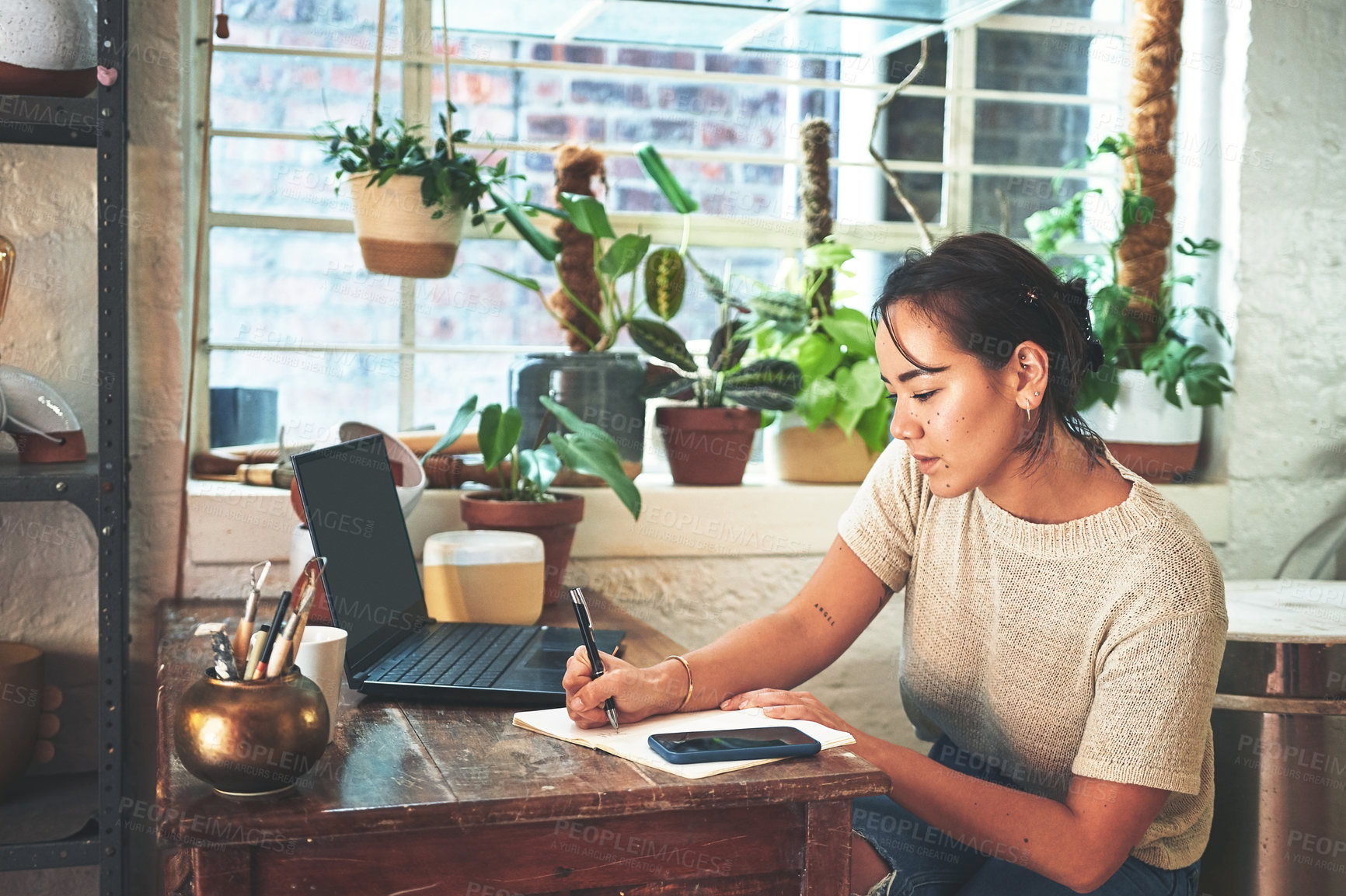 Buy stock photo Cropped shot of an attractive young business owner sitting alone in her pottery studio and making notes