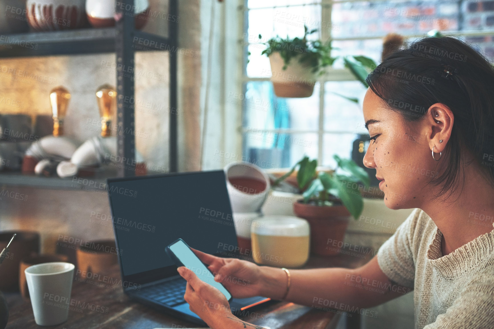 Buy stock photo Cropped shot of an attractive young business owner sitting alone in her pottery studio and using her cellphone