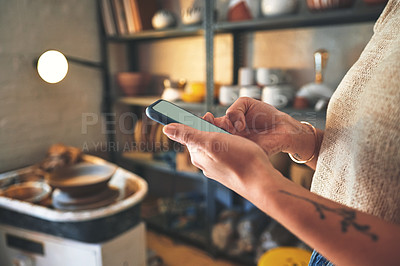 Buy stock photo Cropped shot of an unrecognizable business owner standing alone in her pottery studio and using her cellphone