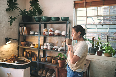 Buy stock photo Cropped shot of an attractive young business owner standing alone in her pottery studio and enjoying a cup of tea