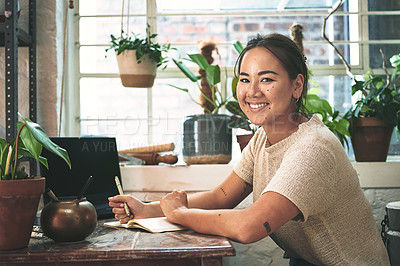 Buy stock photo Cropped portrait of an attractive young business owner sitting alone in her pottery studio and making notes
