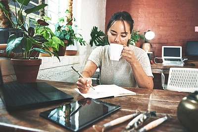 Buy stock photo Cropped shot of an attractive young businesswoman sitting in her pottery studio and writing while enjoying a cup of coffee