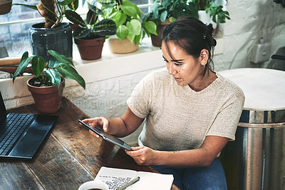 Buy stock photo Cropped shot of an attractive young business owner sitting alone in her pottery studio and using a tablet