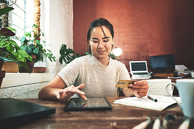 Buy stock photo Cropped shot of an attractive young business owner sitting alone in her studio and using a tablet for online shopping