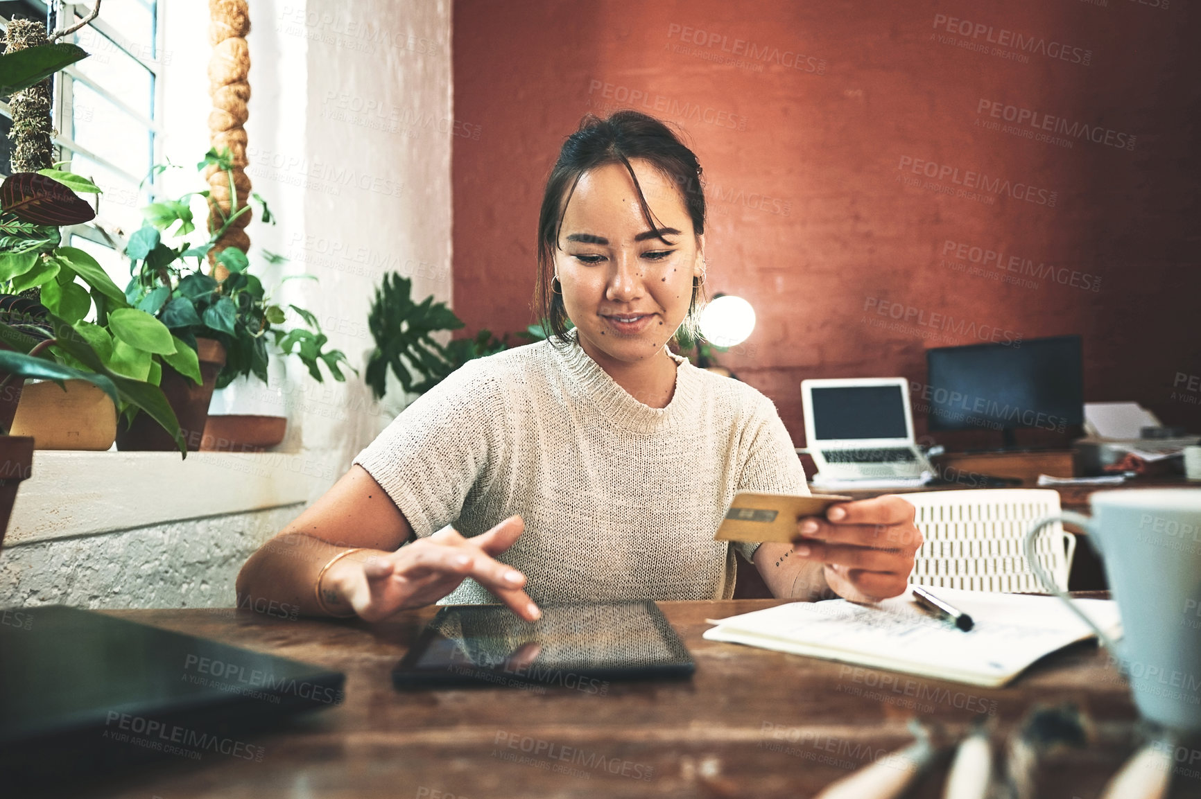 Buy stock photo Cropped shot of an attractive young business owner sitting alone in her studio and using a tablet for online shopping