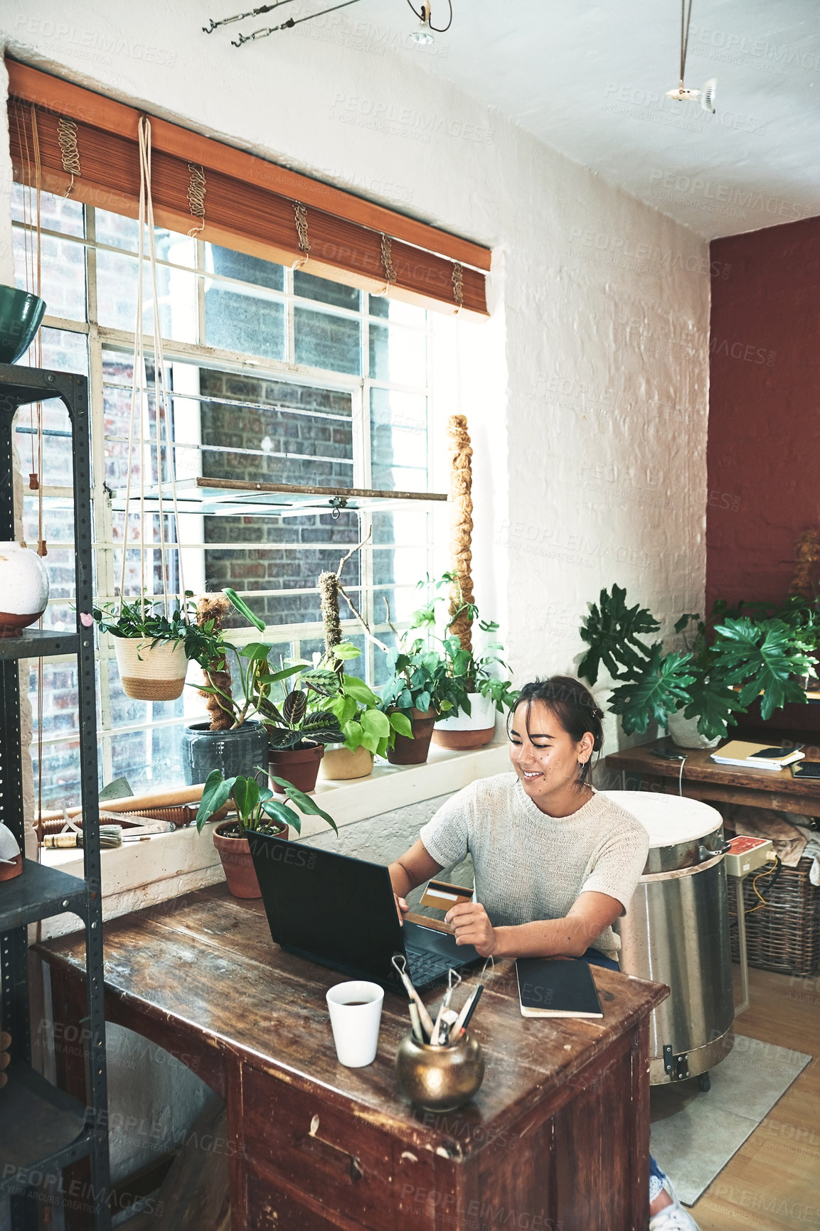 Buy stock photo Cropped shot of an attractive young business owner sitting alone in her studio and using a laptop for online shopping