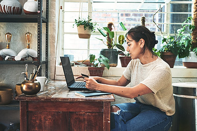 Buy stock photo Cropped shot of an attractive young business owner sitting alone in her studio and using a laptop for online shopping