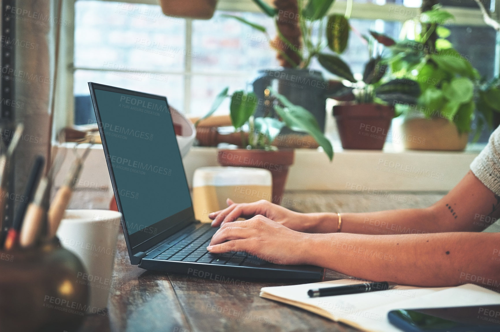 Buy stock photo Cropped shot of an unrecognizable business owner sitting alone in her pottery studio and using her laptop