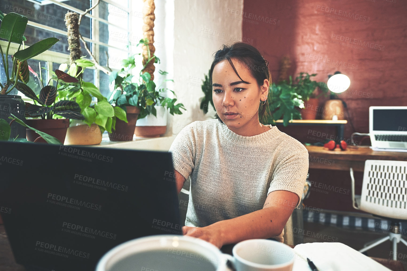 Buy stock photo Cropped shot of an attractive young business owner sitting alone in her pottery studio and using her laptop