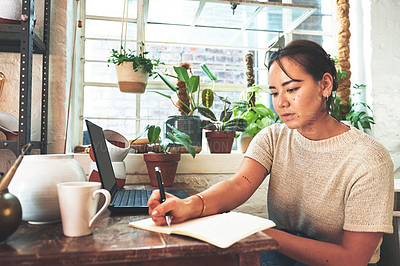Buy stock photo Cropped shot of an attractive young business owner sitting alone in her pottery studio and making notes