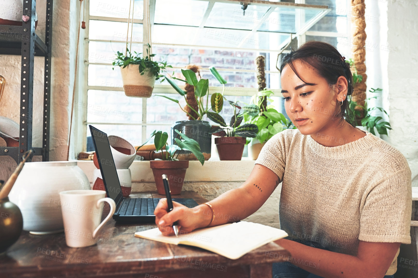 Buy stock photo Cropped shot of an attractive young business owner sitting alone in her pottery studio and making notes