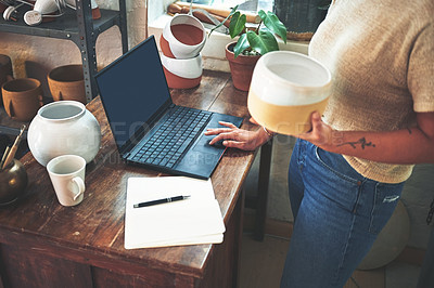 Buy stock photo Cropped shot of an unrecognizable business owner standing and holding a clay pot while using her laptop