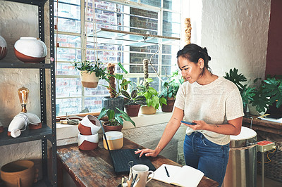 Buy stock photo Cropped shot of an attractive young business owner standing and using her laptop and cellphone in her pottery studio
