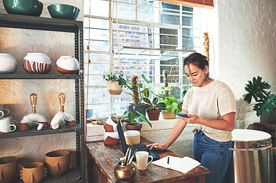 Buy stock photo Cropped shot of an attractive young business owner standing and using her laptop and cellphone in her pottery studio