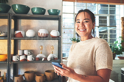 Buy stock photo Cropped portrait of an attractive young business owner standing alone in her pottery studio and using her cellphone