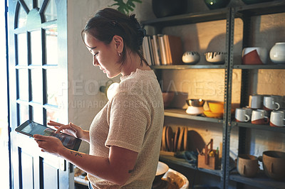 Buy stock photo Cropped shot of an attractive young business owner standing alone in her pottery studio and using a tablet