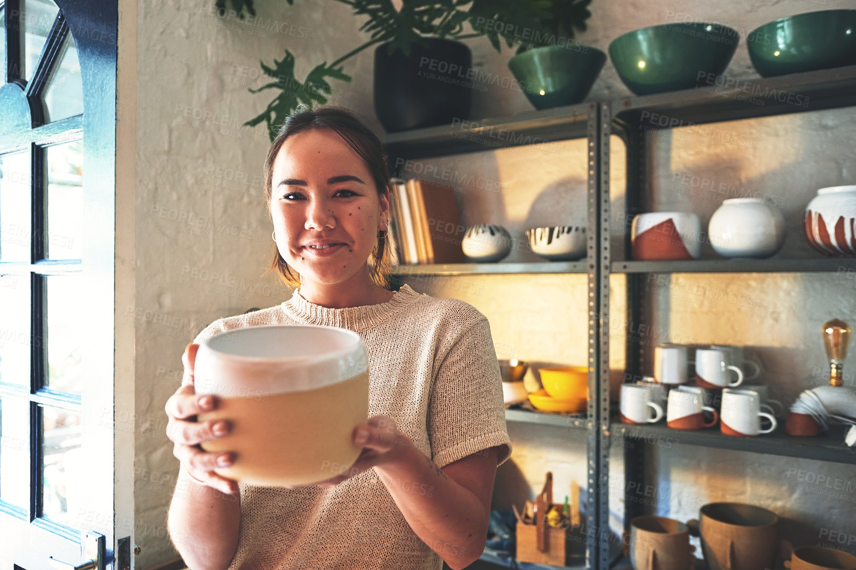 Buy stock photo Cropped portrait of an attractive young business owner standing alone and holding a clay pot in her pottery studio