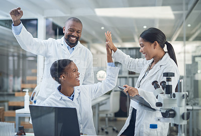 Buy stock photo Shot of a group of young scientists giving each other a high five while using a laptop in a laboratory