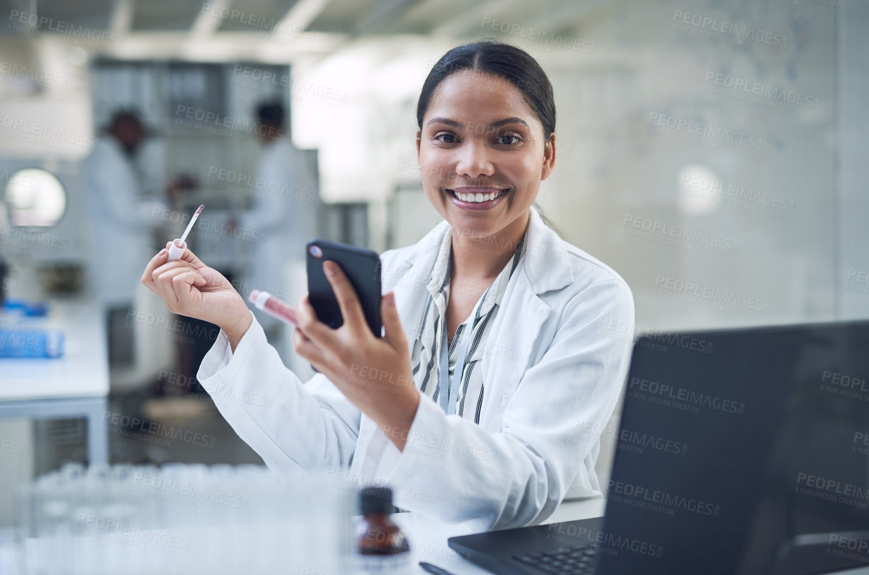 Buy stock photo Shot of a young scientist applying makeup using a smartphone while conducting research in a laboratory