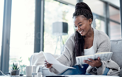Buy stock photo Shot of a young woman going over paperwork on the sofa at home
