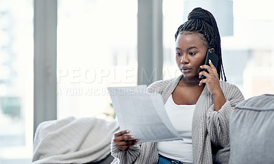 Buy stock photo Shot of a young woman going over paperwork and using a smartphone on the sofa at home