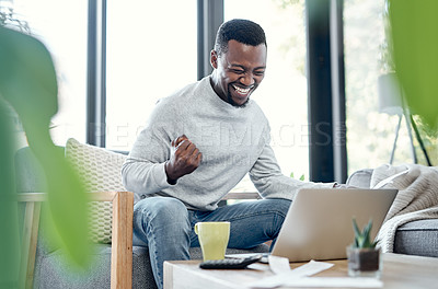 Buy stock photo Shot of a young man celebrating while going over paperwork and using a laptop at home