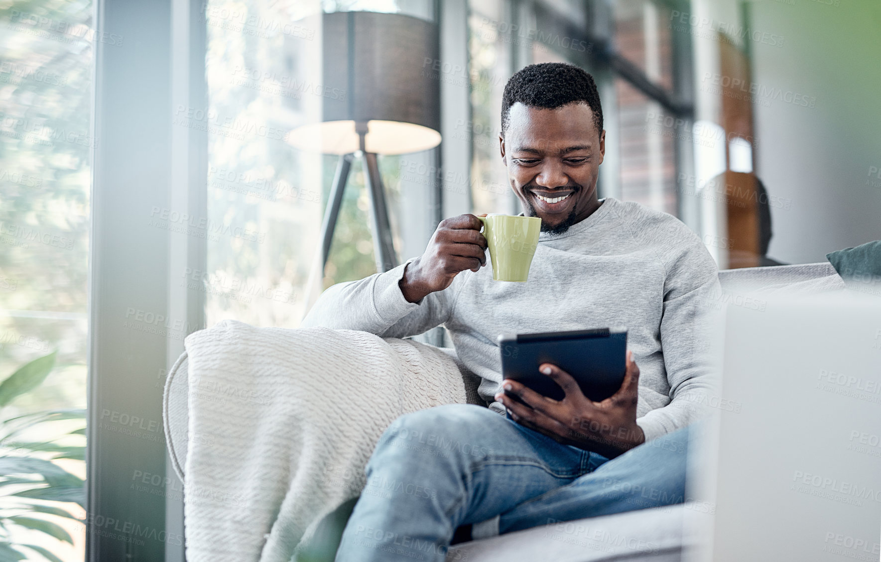 Buy stock photo Relax, coffee and tablet with an african man on a sofa, sitting in the living room of his home to browse social media. Smile, technology or internet with a happy male person relaxing alone in a house