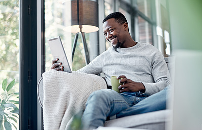 Buy stock photo Relax, coffee and tablet with a black man on a sofa, sitting in the living room of his home to browse social media. Smile, technology and internet with a happy male person relaxing alone in a house