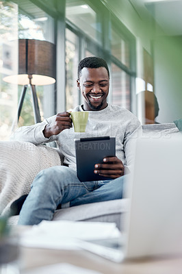 Buy stock photo Shot of a young man using a digital tablet and having coffee on the sofa at home