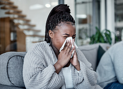 Buy stock photo Shot of a young woman blowing her nose with her husband sitting next to her on the sofa