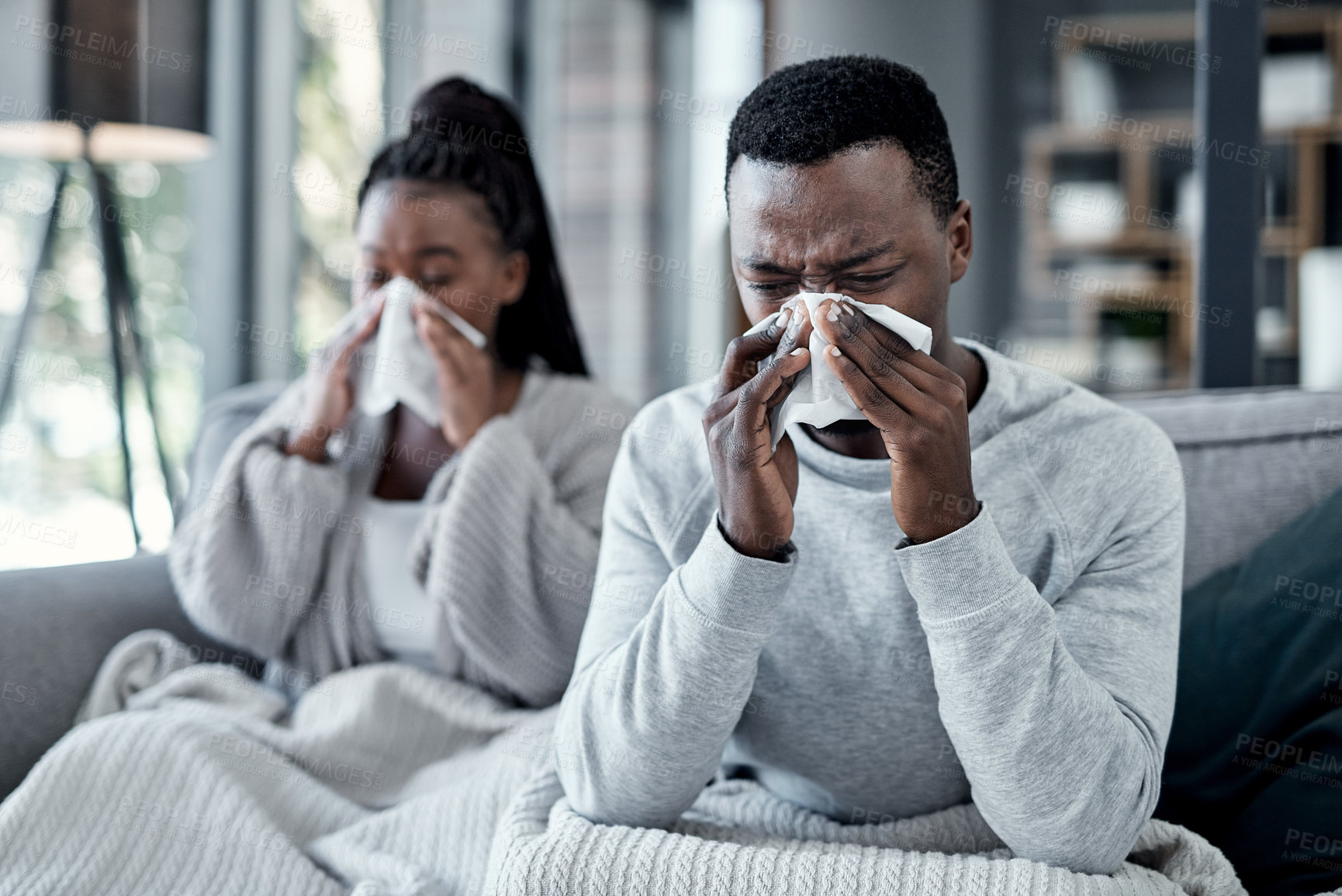 Buy stock photo Shot of a young couple blowing their noses on the sofa at home