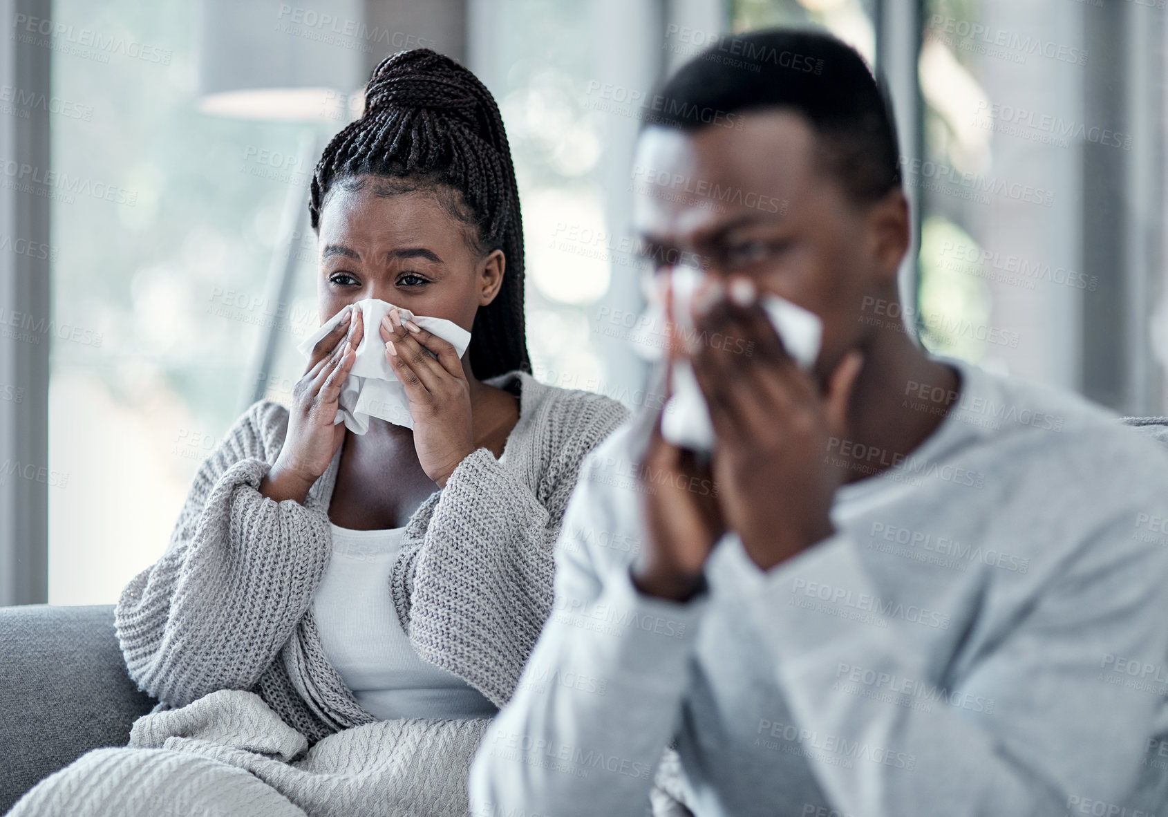 Buy stock photo Shot of a young couple blowing their noses on the sofa at home