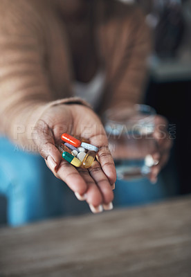 Buy stock photo Cropped shot of an unrecognizable woman sitting alone at home and holding her medication before taking them with water