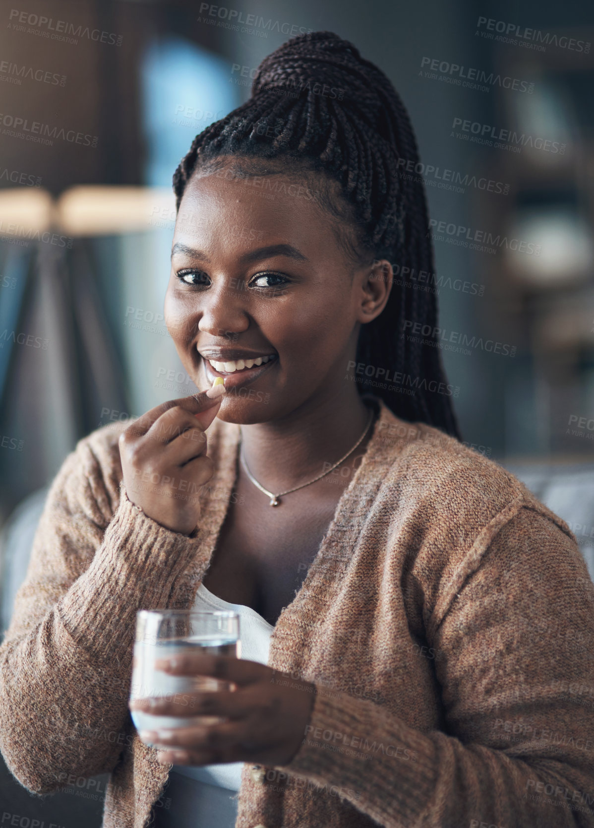 Buy stock photo Cropped shot of an attractive young woman sitting alone and taking her medication with water in her living room