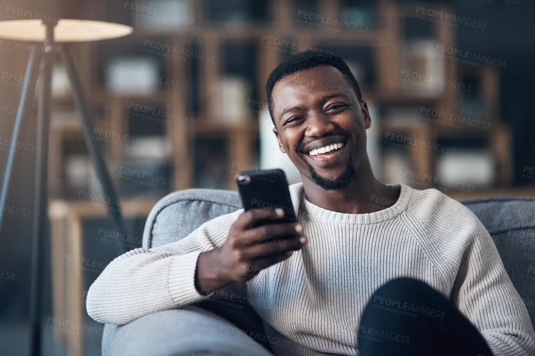 Buy stock photo Cropped shot of a handsome young man sitting alone in his living room and using his cellphone