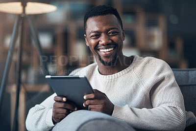 Buy stock photo Cropped shot of a handsome young man sitting alone in his living room and using his tablet