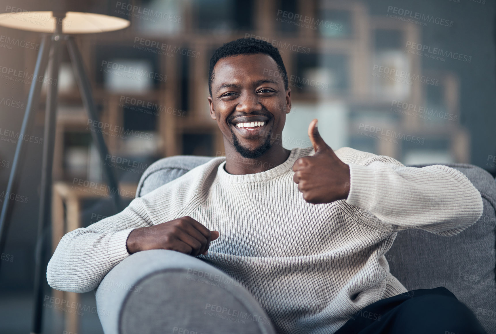 Buy stock photo Cropped shot of a handsome young man sitting alone and making a thumbs-up gesture in his living room