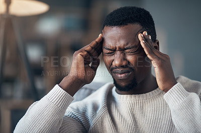 Buy stock photo Cropped shot of a handsome young man sitting alone in his living room and suffering from a headache