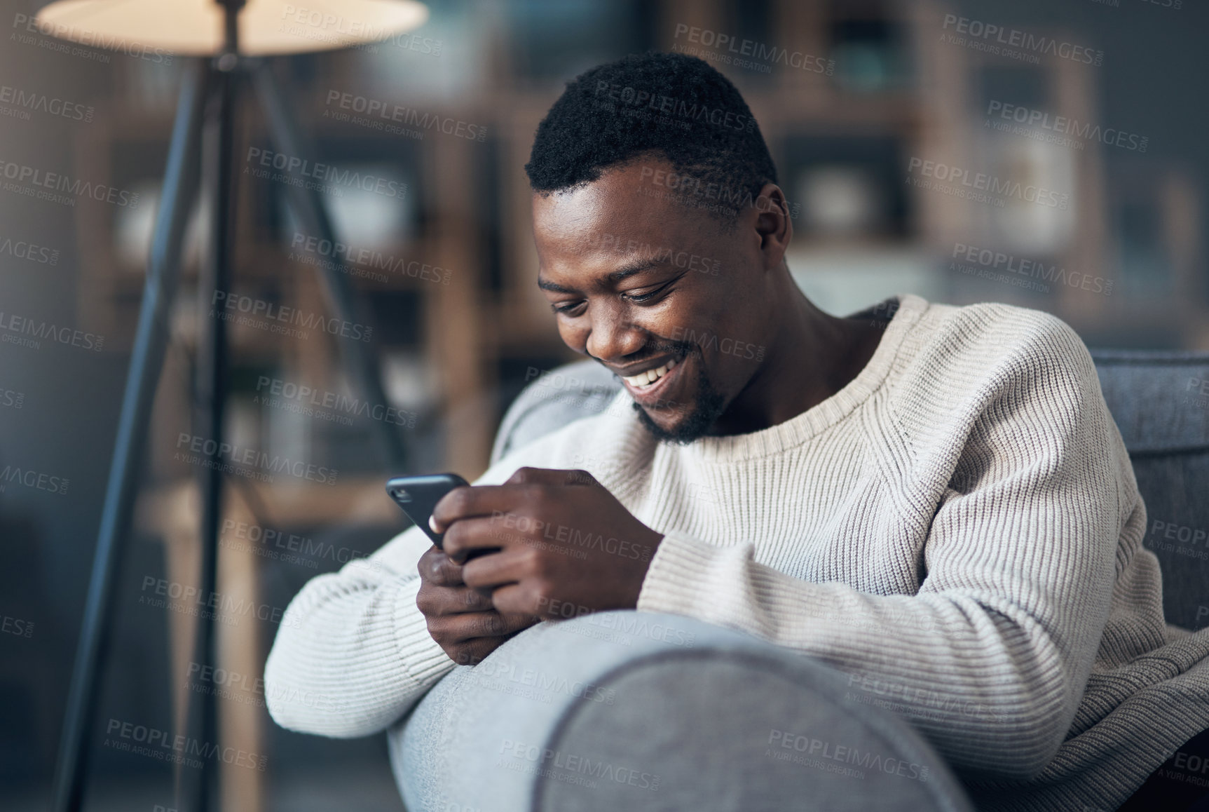 Buy stock photo Cropped shot of a handsome young man sitting alone in his living room and using his cellphone