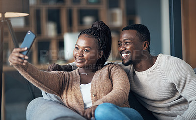 Buy stock photo Cropped shot of a happy young couple sitting together and using a cellphone to take a selfie at home