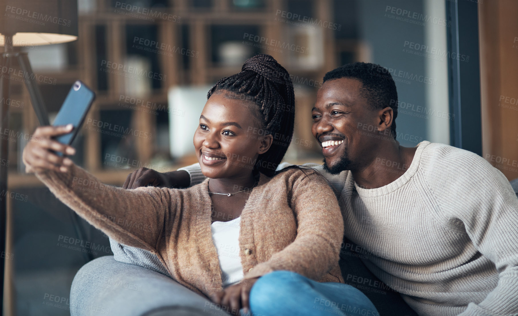 Buy stock photo Cropped shot of a happy young couple sitting together and using a cellphone to take a selfie at home