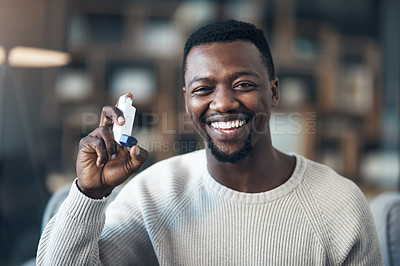 Buy stock photo Cropped shot of a handsome young man sitting alone in his living room and holding his asthma pump