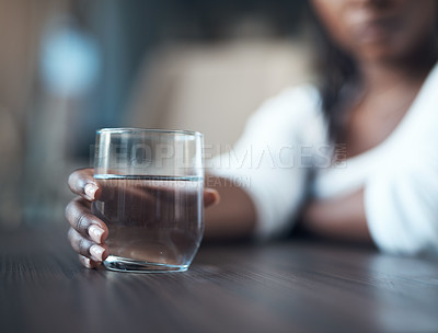Buy stock photo Cropped shot of an attractive young woman sitting alone and holding a glass of water at home