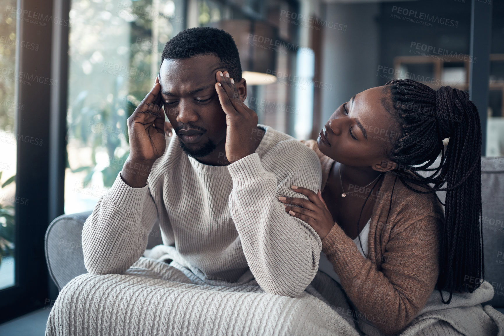 Buy stock photo Cropped shot of a handsome young man sitting and suffering from a headache while his girlfriend comforts him at home