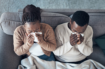 Buy stock photo High angle shot of a young couple sitting in their living room together and feeling sick while blowing their nose