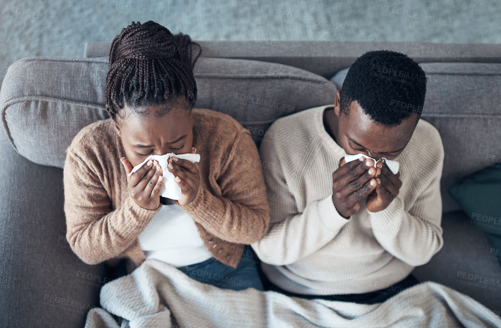 Buy stock photo High angle shot of a young couple sitting in their living room together and feeling sick while blowing their nose