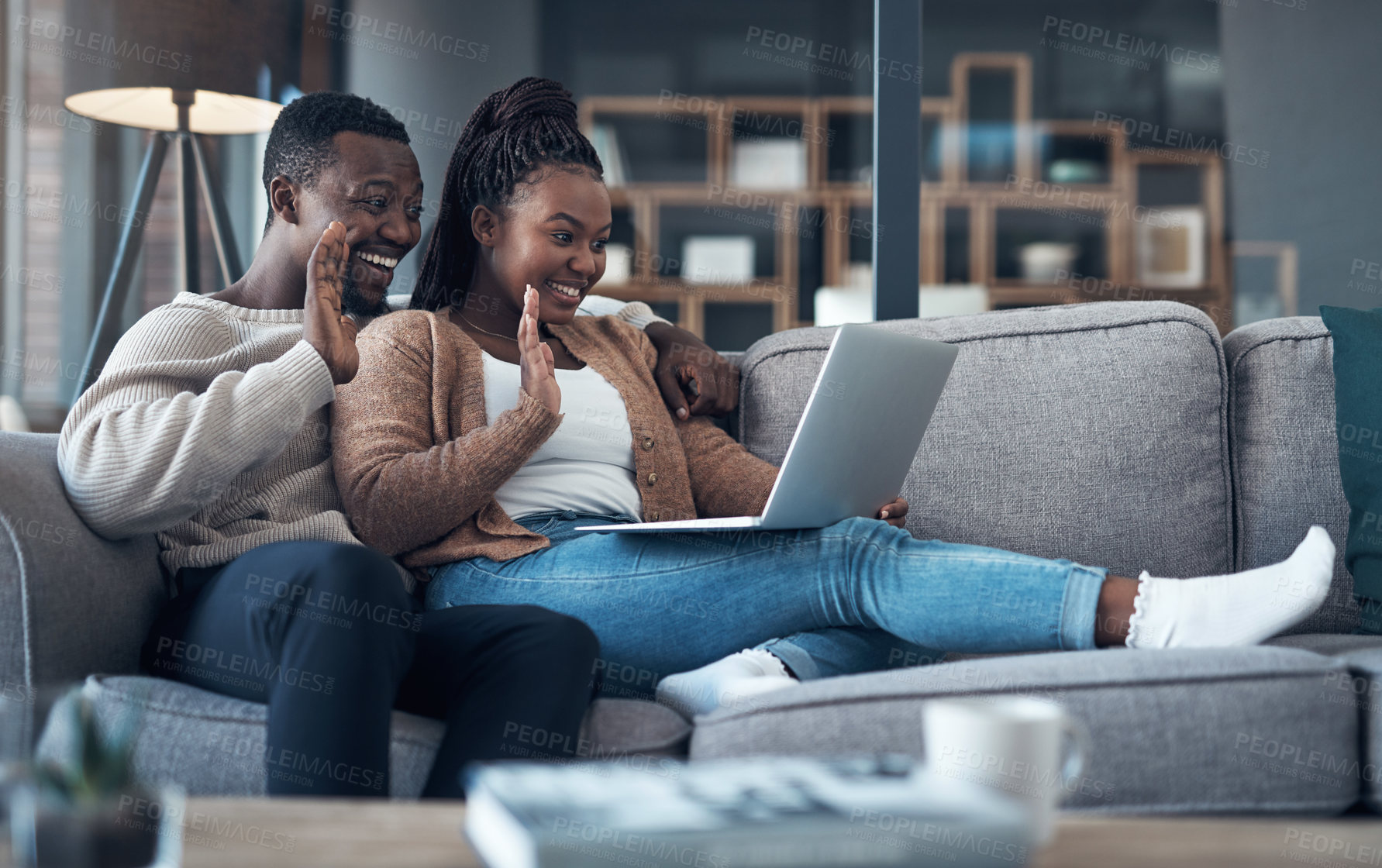 Buy stock photo Cropped shot of a happy young couple sitting together on their sofa and using a laptop for a video chat